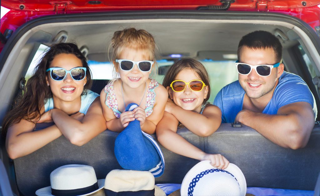 Portrait of a smiling family with two children at beach in the car. Holiday and travel concept